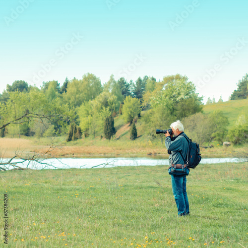 Elderly man travels in wildlife. Portrait of the gray-haired traveler in background of the landscape. Old photographer enjoys traveling and photography