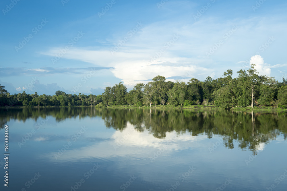 Scenic view of lake with lush tropical greenery reflecting under bright Asian sky in the moat at Angkor Wat, Cambodia