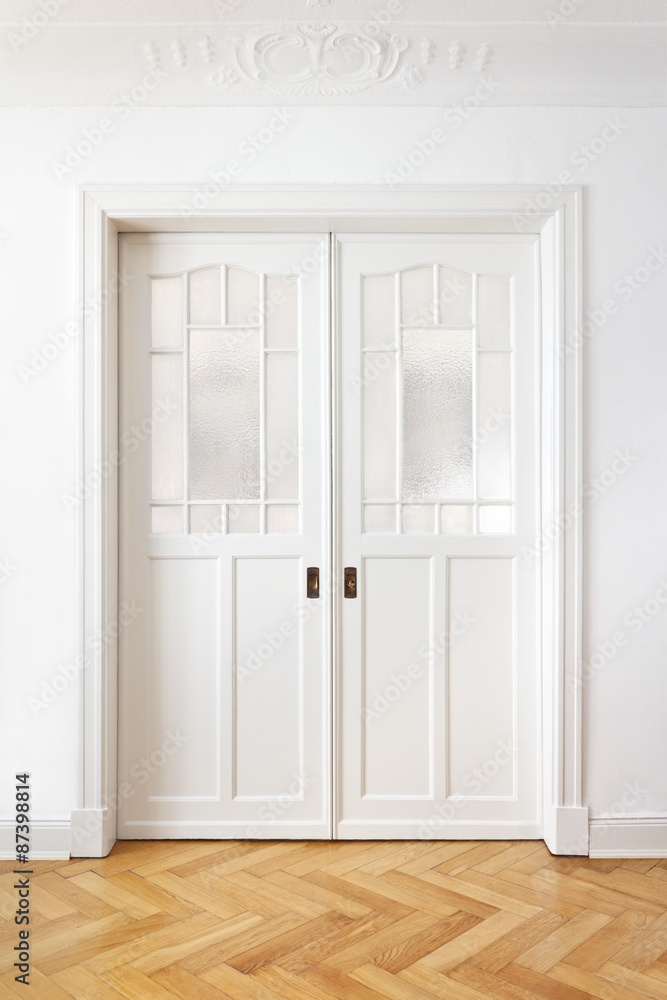 White old double sliding or pocket doors with textured glass in an old building with crown moldings. White old double sliding or pocket doors with textured glass in an old building with crown moldings.