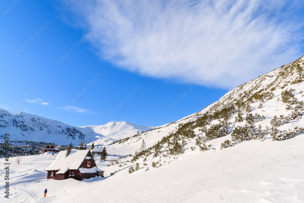 Backpacker in front of wooden mountain hut in winter landscape of Gasienicowa valley, Tatra Mountains, Poland