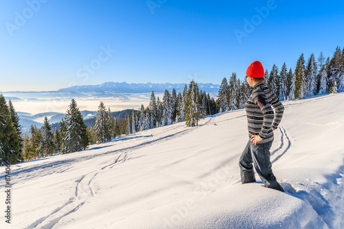 Young woman tourist standing in deep snow in Gorce Mountains looking at distant Tatry Mountains panorama, Poland