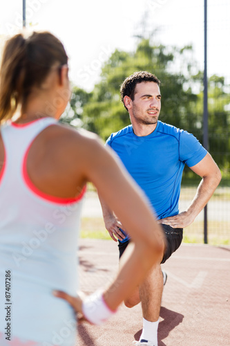 Young athletic man and woman stretching outdoors on a hot summer