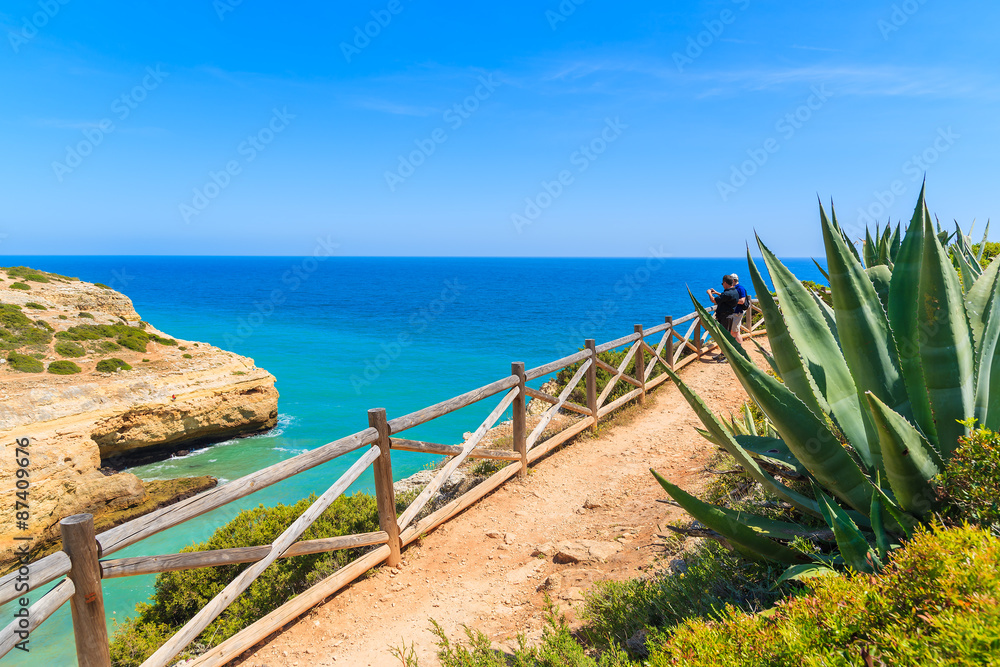 Tourists on cliff path along sea watching beautiful sea bay near Carvoeiro town, Portugal