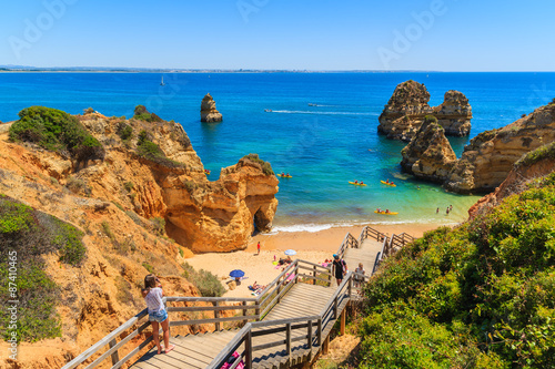 Unidentified young woman tourist taking photo of beautiful beach Praia do Camilo, Portugal