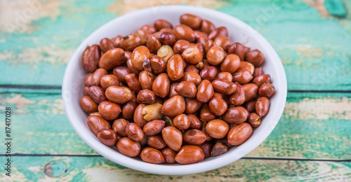 Deep fried peanuts in white bowl over rustic wooden background