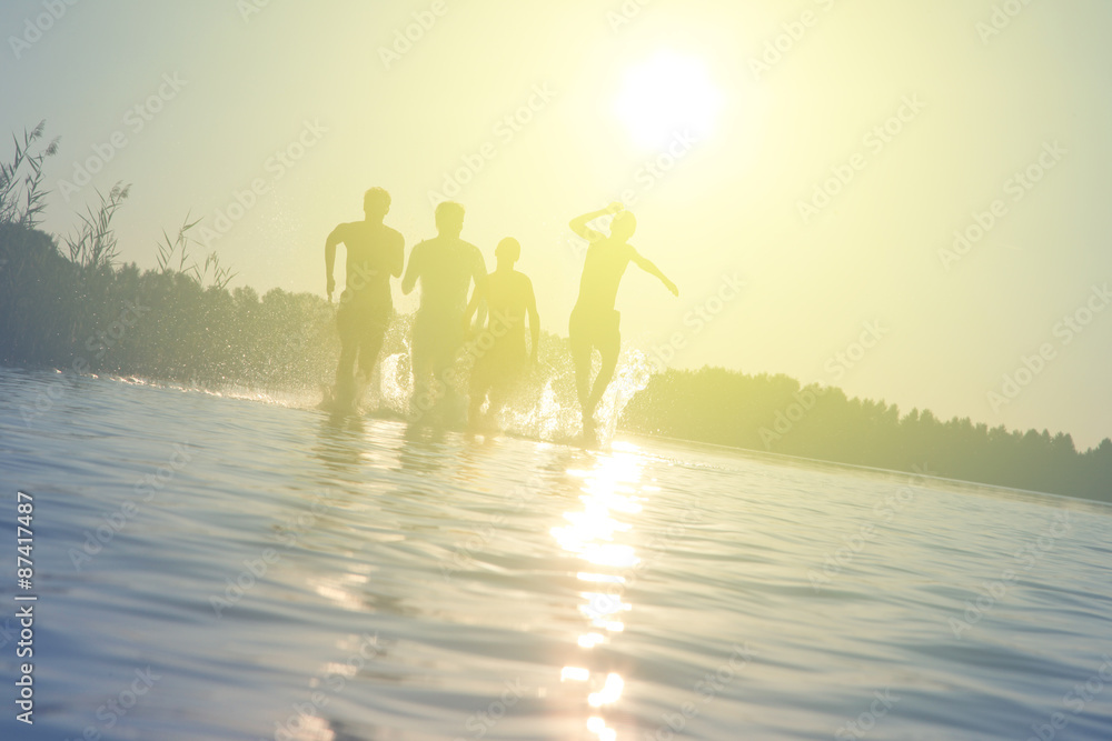 Fototapeta premium Glückliche junge Menschen laufen und springen am See beim Sonnenuntergang