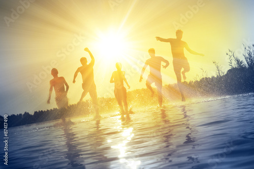 Gl  ckliche junge Menschen laufen und springen am See beim Sonnenuntergang
