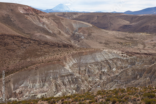 Eroded rock formations at the head of a river valley feeding the River Lauca high up on the Altiplano of northern Chile in Lauca National Park.  On the horizon is the Parinacota volcano (6342m).