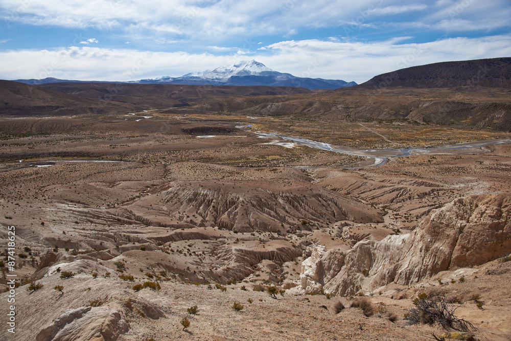 Eroded rock formations at the head of a river valley feeding the River Lauca high up on the Altiplano of northern Chile in Lauca National Park.  In the background is the Guallatiri volcano (6063 m).