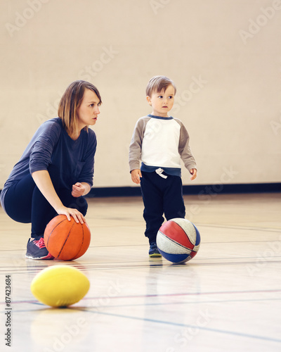 Mother and son playing with ball in gym, early child healthy development, family fun, coaching and training concept,