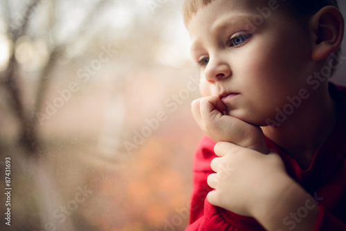 small boy sitting near window and thnking about something