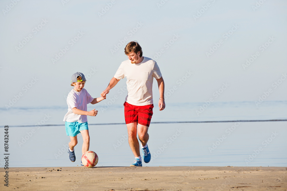 Happy father and son play soccer or football on the beach Happy father and son play soccer or football on the beach