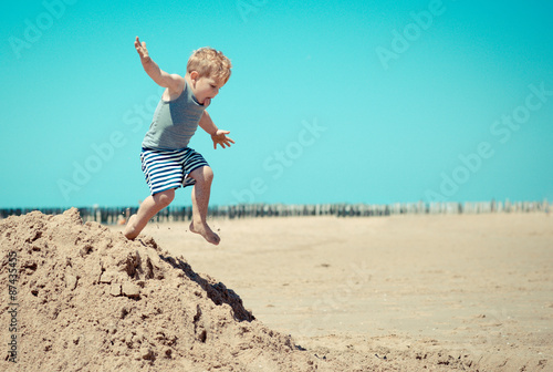 Little boy child jumps from a mountain on the beach