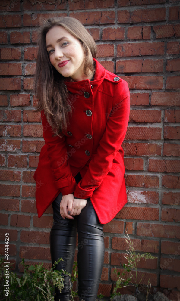 Beautiful girl in a red coat on brick wall background Beautiful girl in a red coat on brick wall background