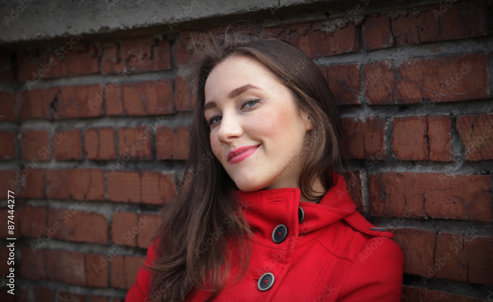 Portrait of a beautiful girl in a red coat on a brick wall backg