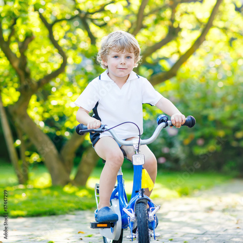 Little preschool kid boy riding with bicycle in summer