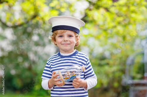 Happy kid in skipper uniform playing with toy ship