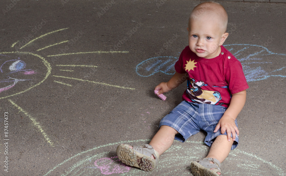 Naklejka premium little boy draws with chalk on the pavement sun