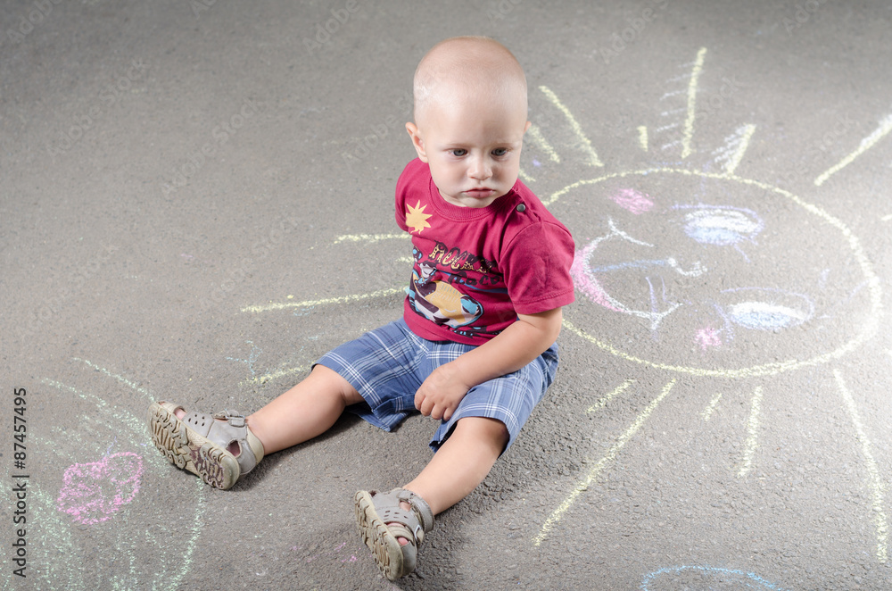 Naklejka premium little boy draws with chalk on the pavement sun