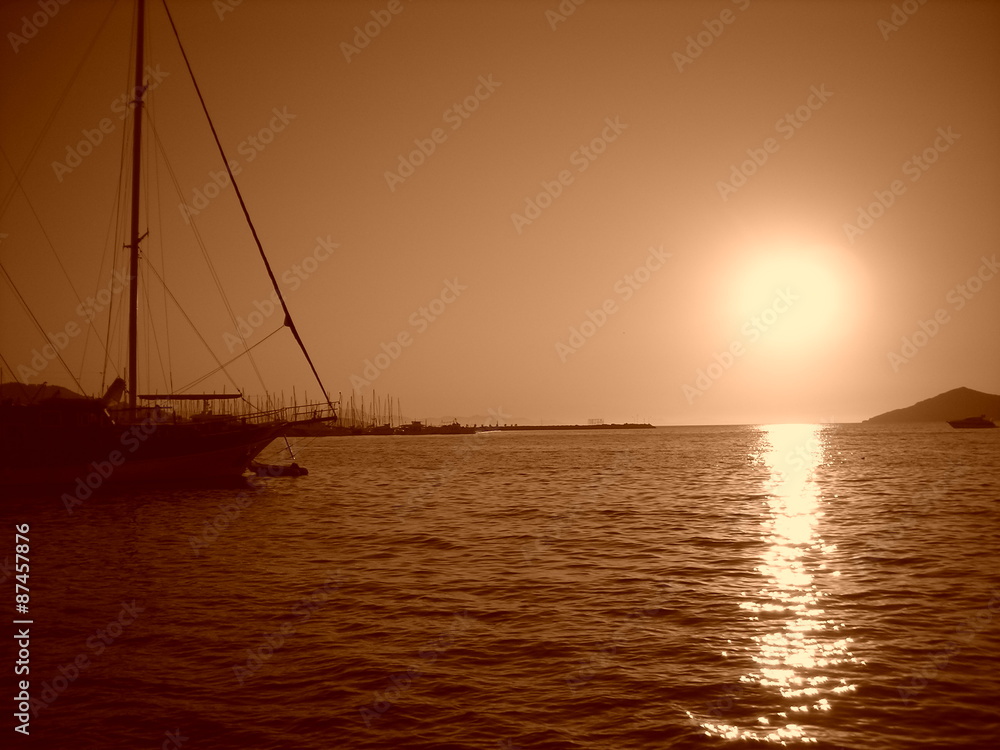 Summer sunset at sea with moored boat; monochrome. Image filtered in faded, washed out, retro style with sepia filter; nostalgic summer vintage concept.