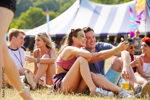 Friends sitting on the grass taking selfie at music festival