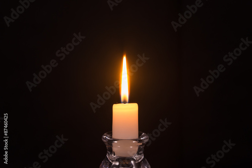 Burning white candle on a black background