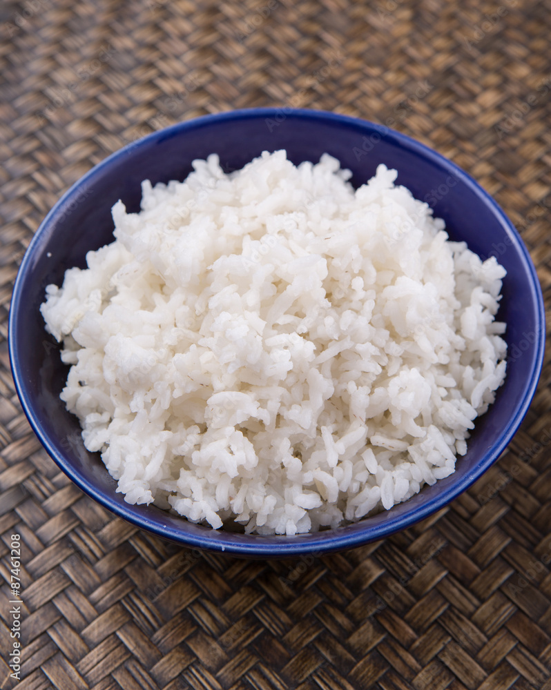 Cooked steamed rice in a blue bowl over wicker background Cooked steamed rice in a blue bowl over wicker background