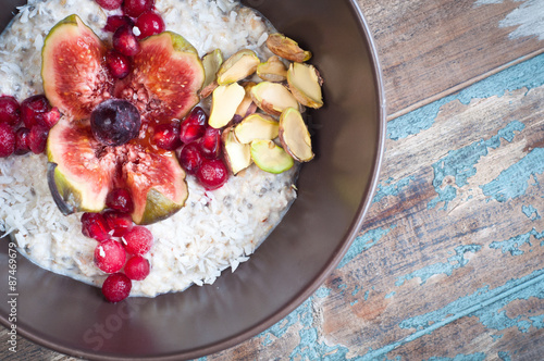 Home made bircher style muesli porridge topped with fresh sliced fig, pomegranate seeds, pistachio nuts coconut,chia seeds and a cherry. Served on a rustic wooden table.