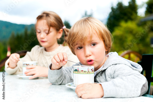 Adorable children drinking hot chocolate outdoors, spending good time on vacation in alpine mountains