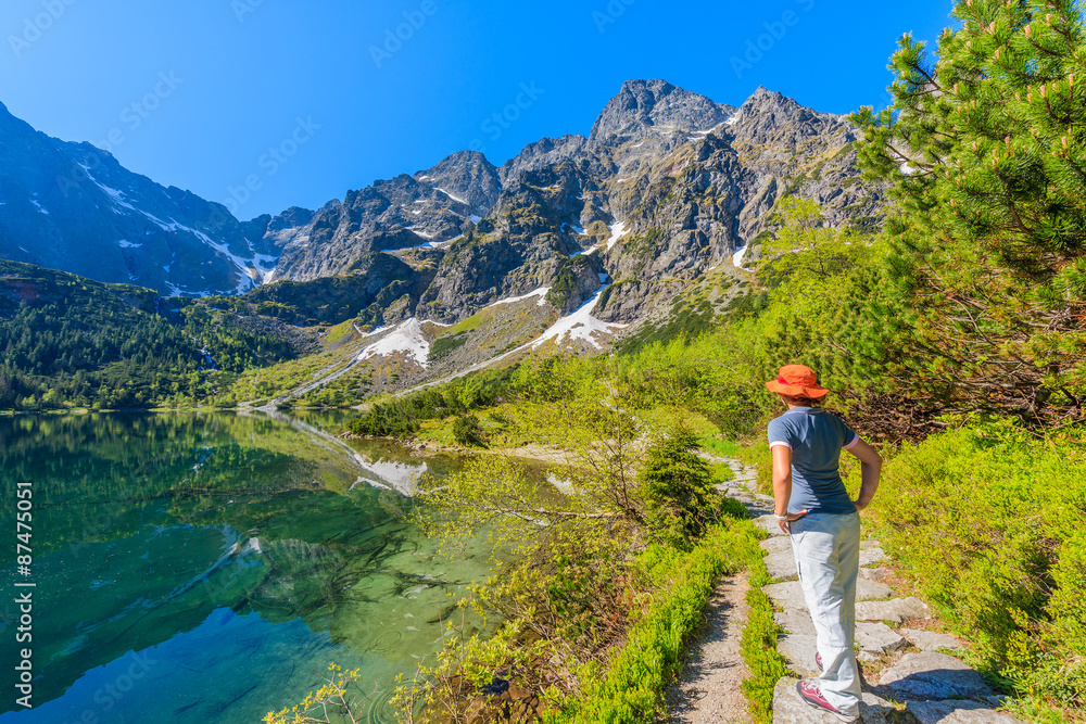 Woman tourist standing on path along beautiful green water Morskie Oko lake, Tatra Mountains, Poland