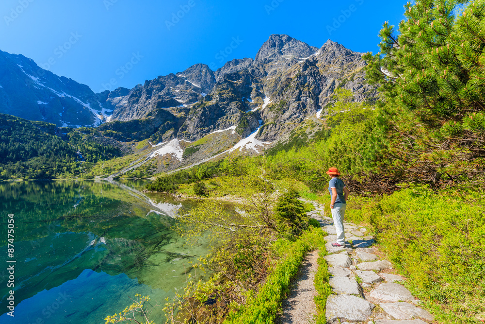 Woman tourist standing on path along beautiful green water Morskie Oko lake, Tatra Mountains, Poland