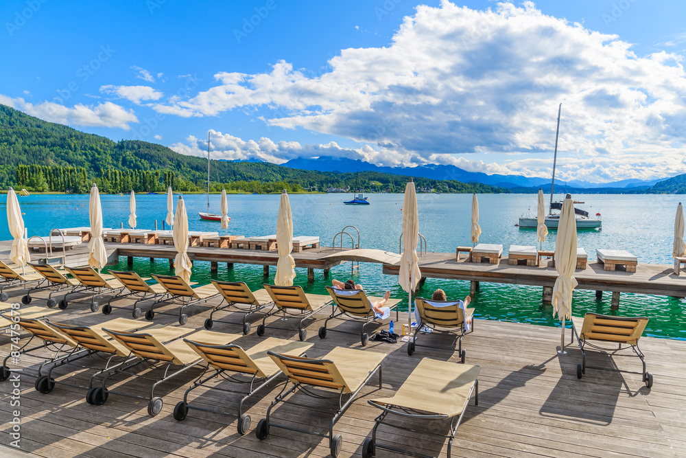 Sunchairs on wooden deck and view of beautiful alpine lake Worthersee in summer, Austria