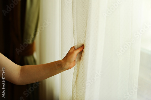 Hand pulling a window curtain