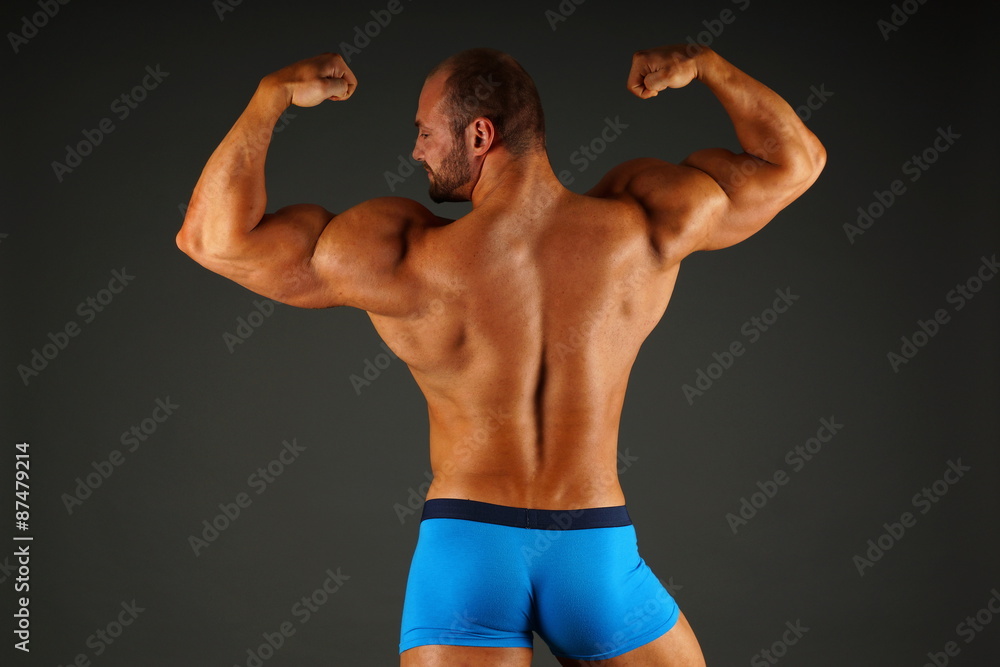 Big muscular man shows his back on gray background