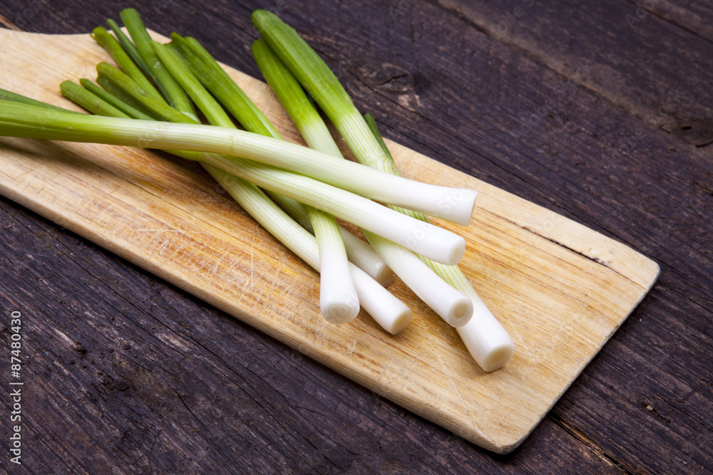 Scallions bunch cleaned and prepared on a wooden board and chopping board shot at an angle on a wooden background Scallions bunch cleaned and prepared on a wooden board and chopping board shot at an angle on a wooden background