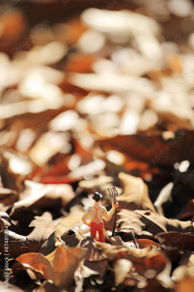 Farmer(miniature) with a fork standing , field of autumnal leaves in a garden. Shallow depth of field composition
