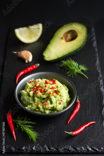 Guacamole dip and ingredients on black background
