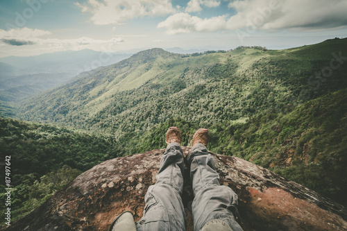 Legs of a man sitting on the edge of a cliff in the beautiful mountains