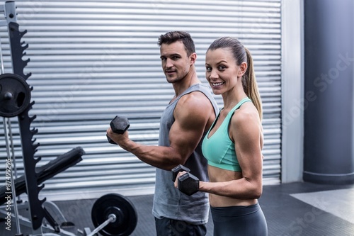 A muscular couple lifting dumbbells