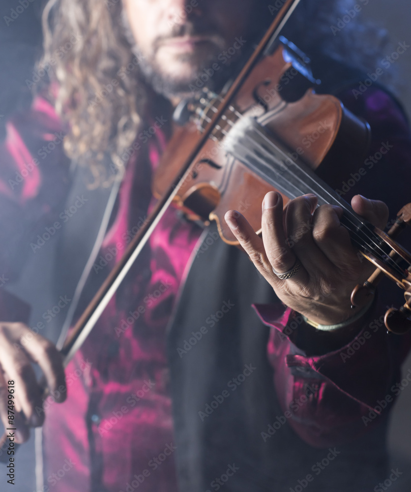 Fototapeta premium handsome man playing classical violin through blue smoke