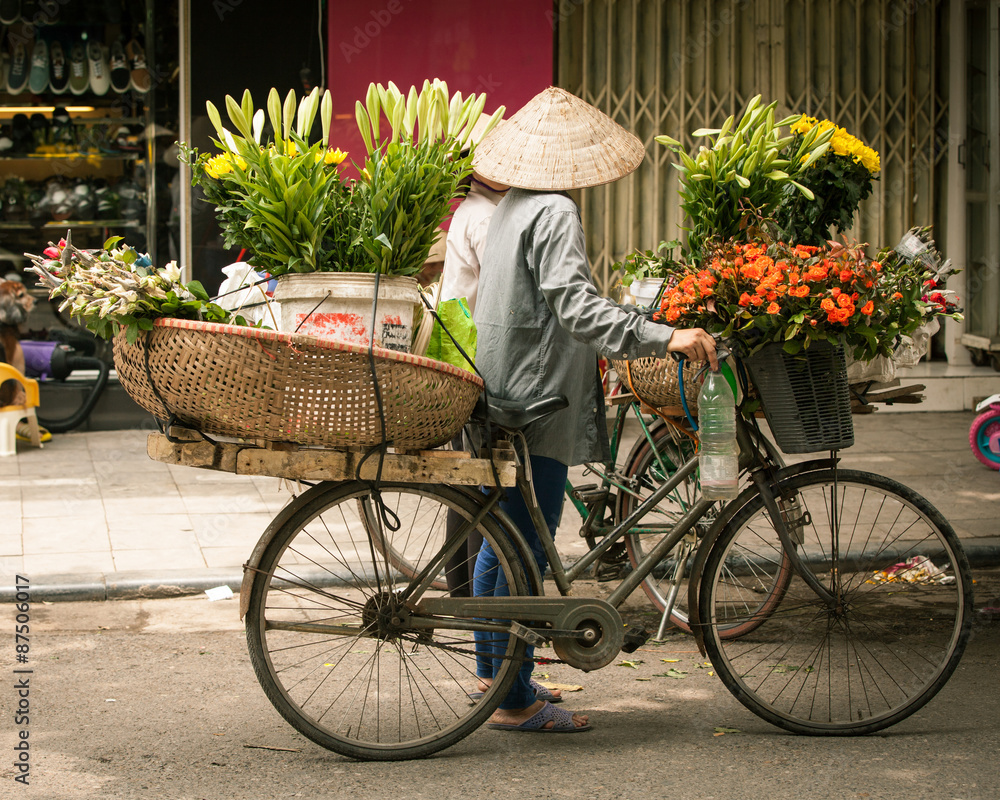 Two women flower vendors in conical hat with bicycle having a conversation on the street of Old Quarter, Hanoi, Vietnam