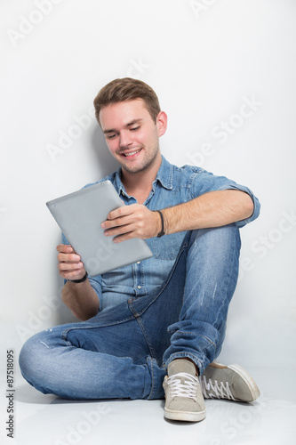 Young caucasian man sitting on the floor holding a tablet pc