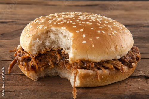 Pulled pork in a bun bitten on a side shot front on on wood