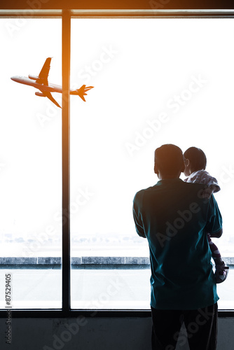 Father holding his baby in airport with airplane on background.