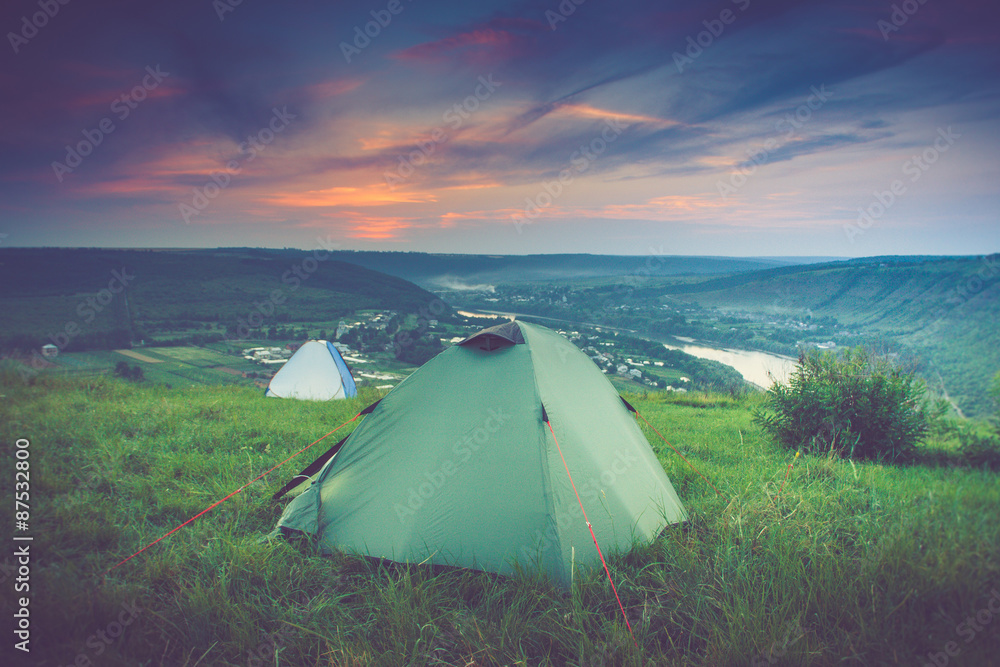 Tourist tent on green meadow at sunset. Camping background.