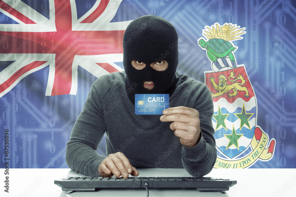 Dark-skinned hacker with flag on background holding credit card - Cayman Islands Dark-skinned hacker with flag on background holding credit card - Cayman Islands