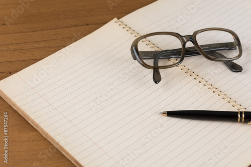 old notebook with pen and glasses on wood table