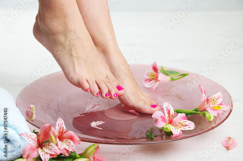 Woman washing beautiful legs in bowl  on light background. Spa procedure concept