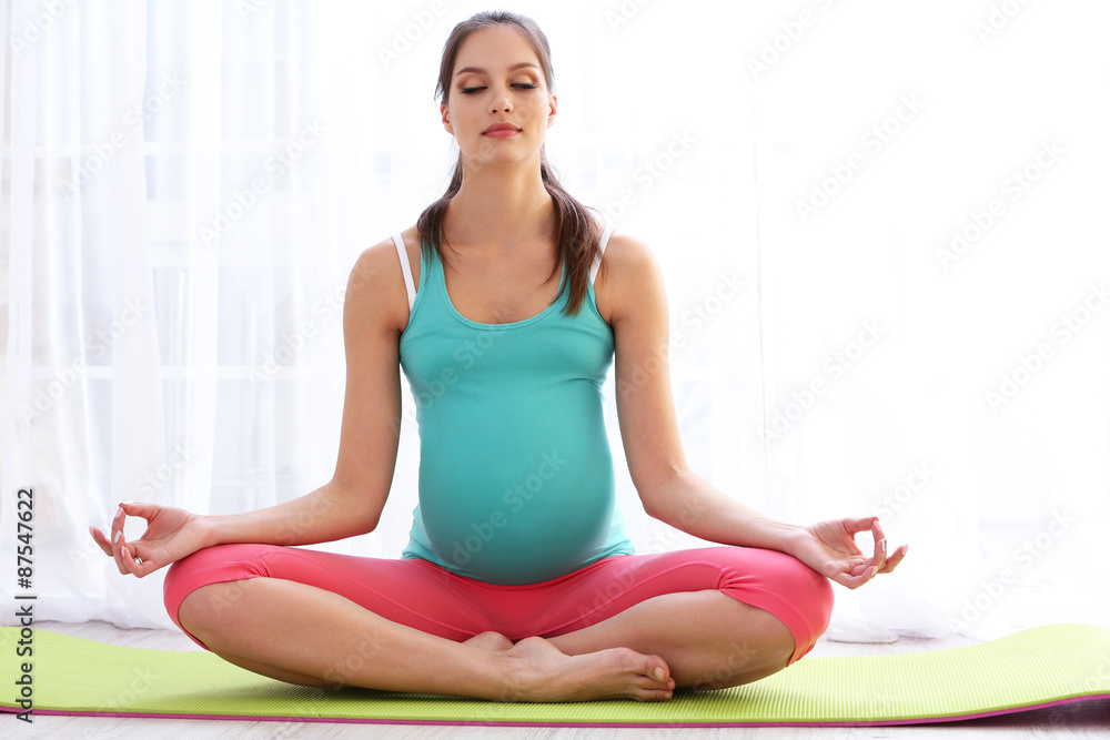 Pregnant woman exercising on green mat in room Pregnant woman exercising on green mat in room