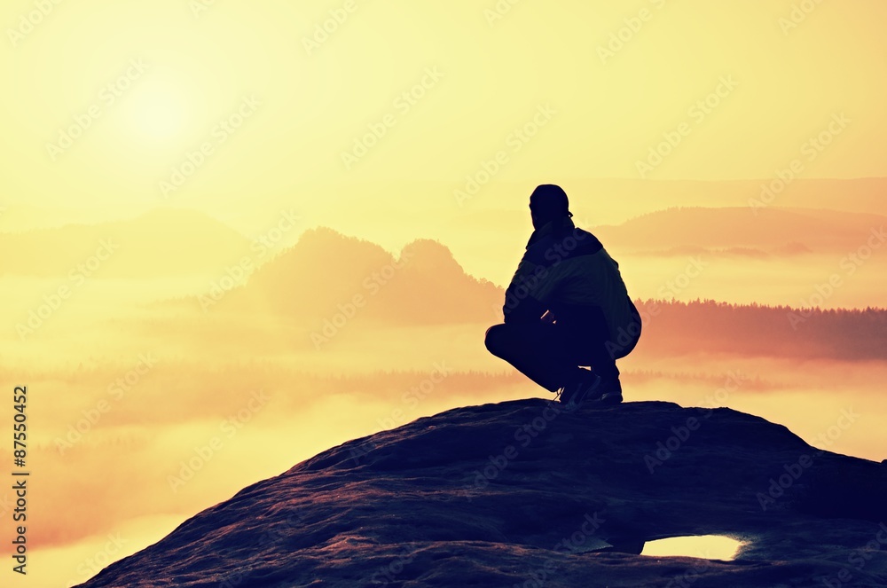 Rear view of male hiker sitting on the rocky peak while enjoying a colorful daybreak above mounrains valley Rear view of male hiker sitting on the rocky peak while enjoying a colorful daybreak above mounrains valley